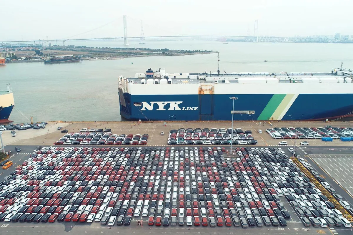 Thousands of export vehicles staged at a Chinese auto terminal beside a car carrier
